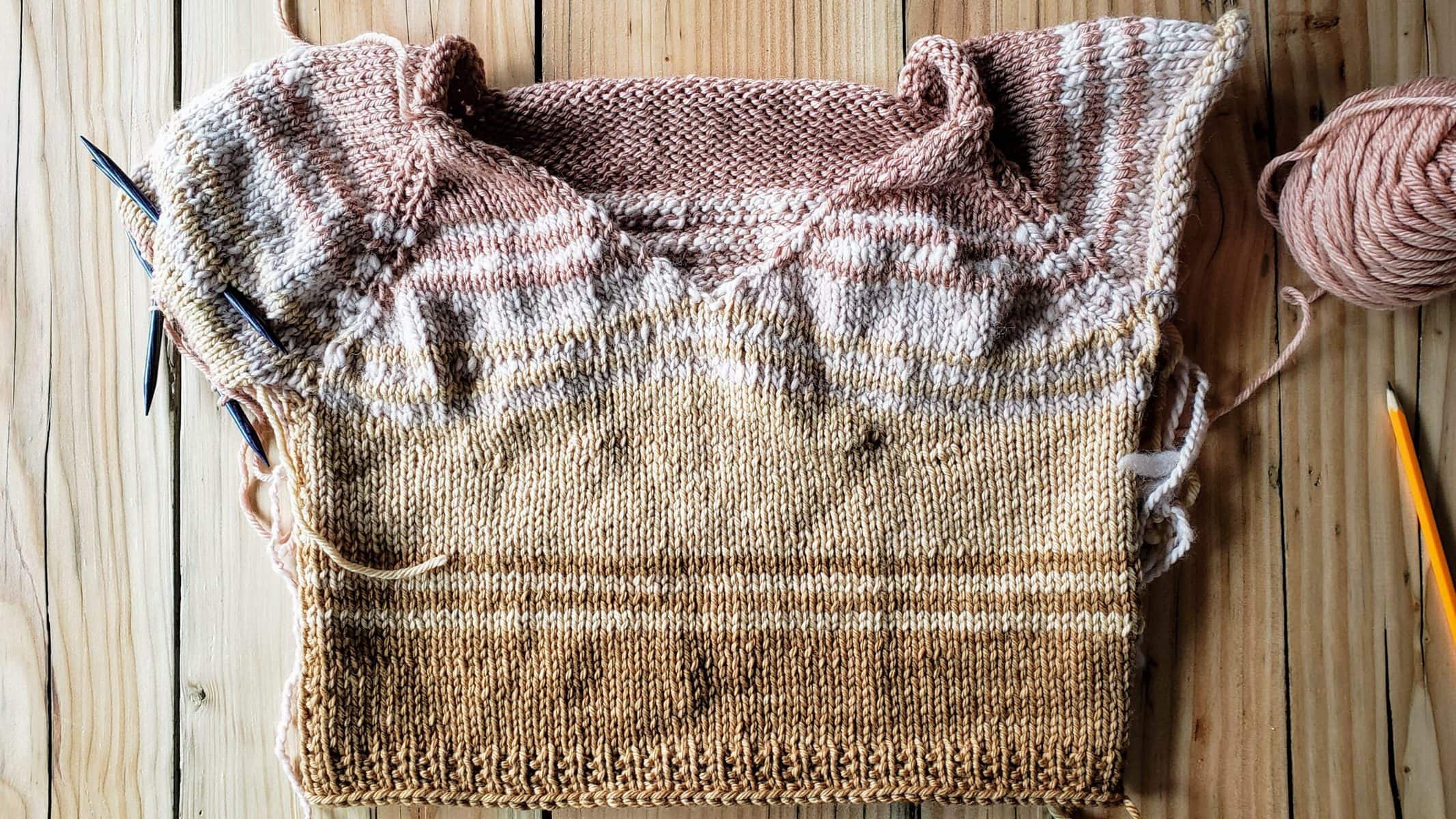 Photo of a striped knitted sweater in progress, made from avocado- and tea-dyed yarns.