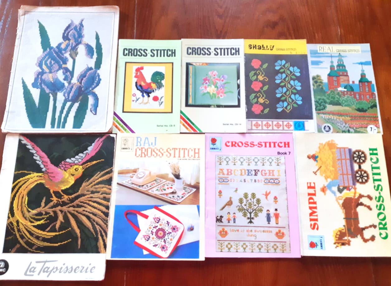 Image description: Nine vintage cross-stitch books laid out in a grid on a table.
