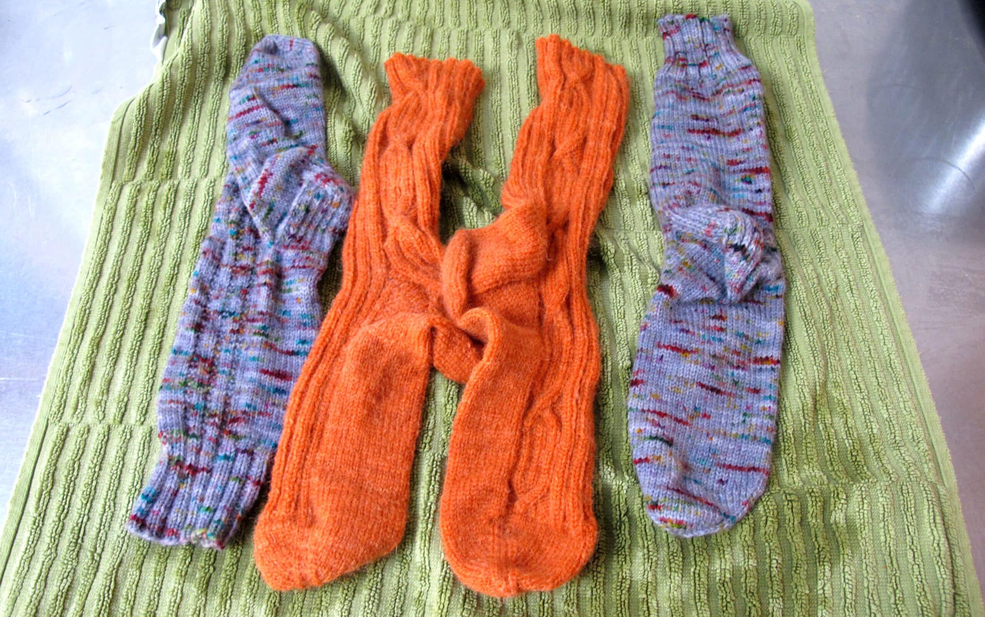 Image description: Four handknit socks laid flat on top of a light-green towel.