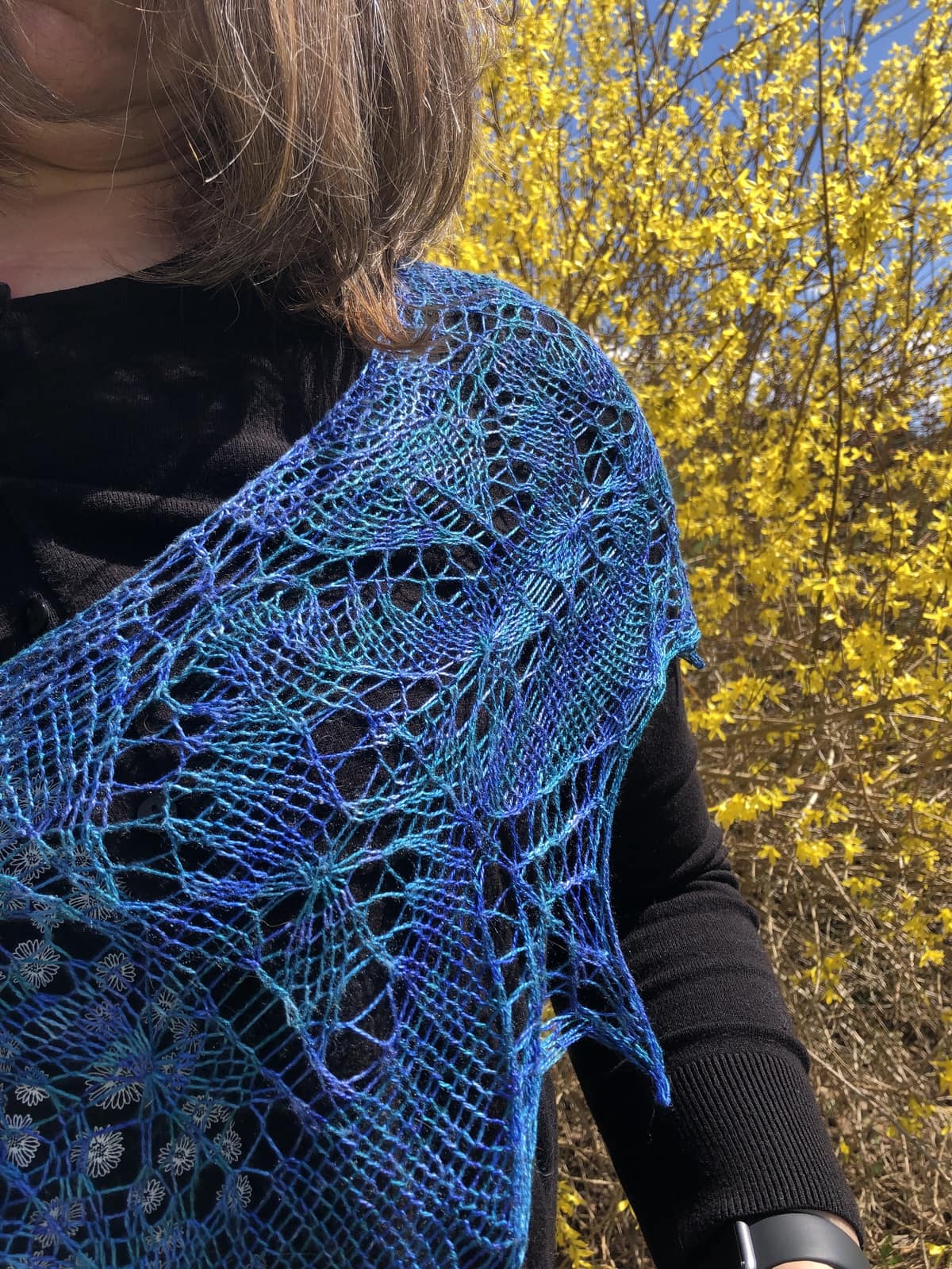image: a blue handknit lace shawl, draped around a woman's shoulders