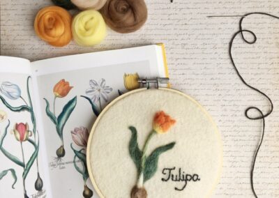 image description: an embroider of a tulip bulb, resting on a book of botanical drawings