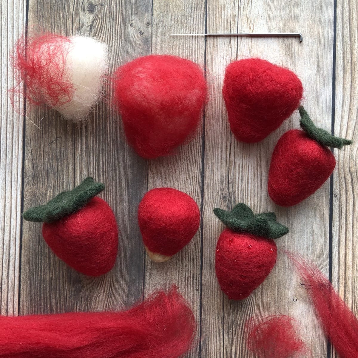 Image description: a collection of needle-felted strawberries in various stages of completion.