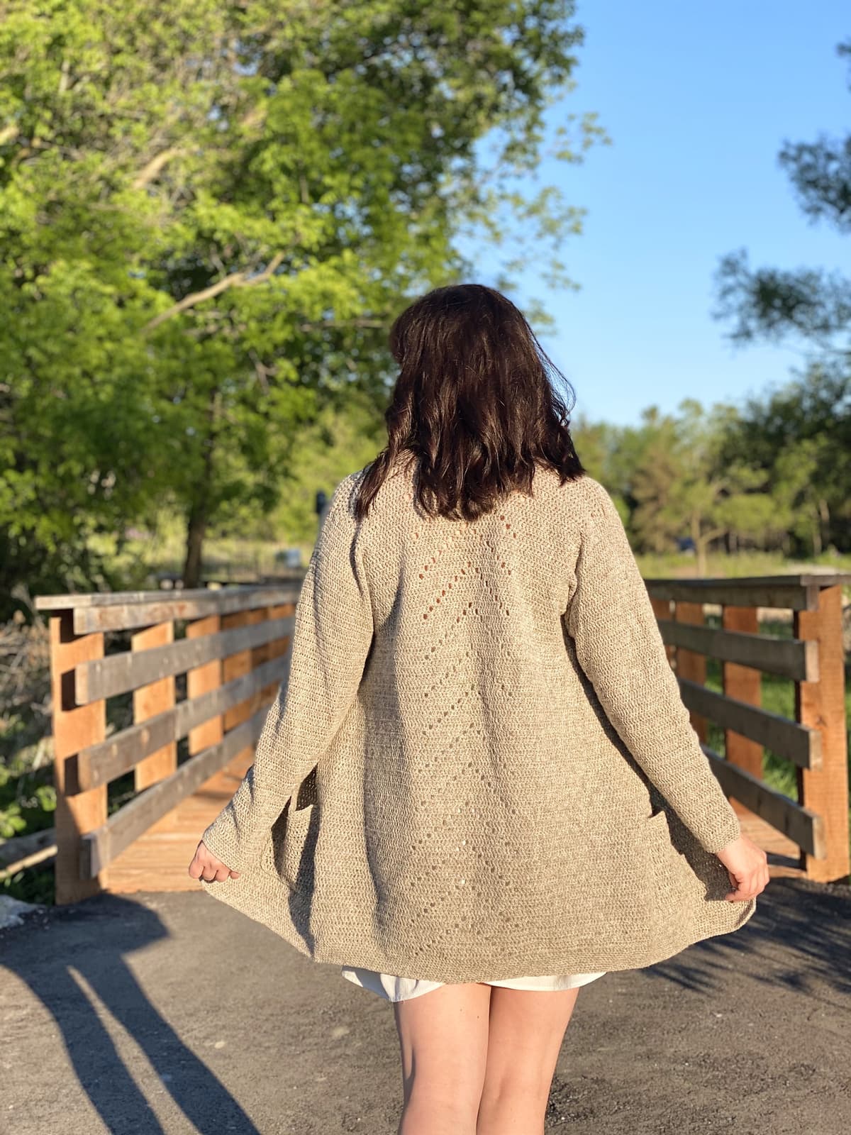 Image description: Woman seen from behind, holding the edges of a cardigan open.