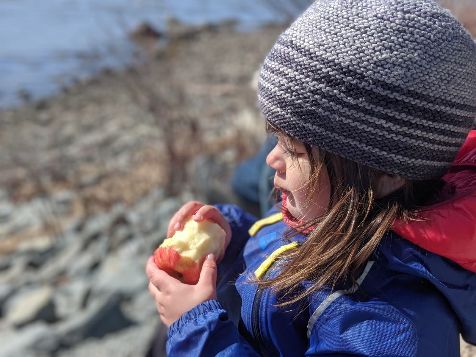 image description: a young child in a handknit hat, holding a partially eaten apple