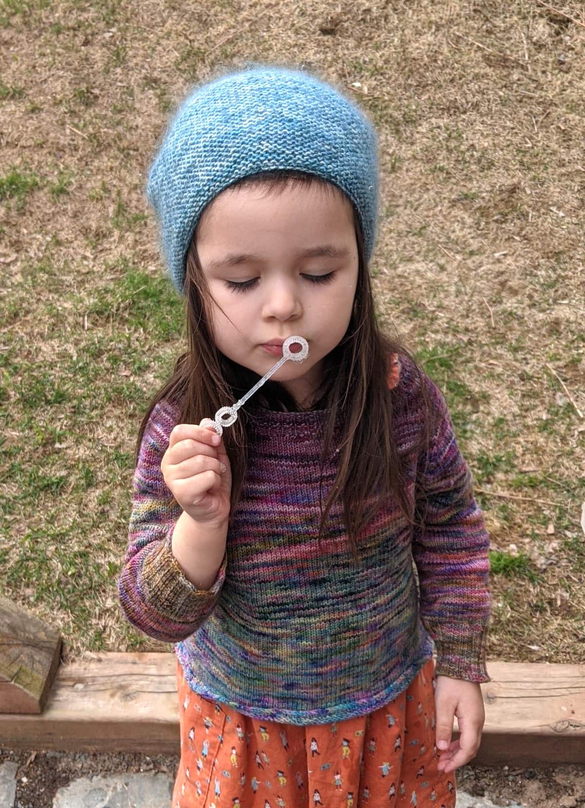 image description: a close-up version of the image to the left, a young child wearing a handknit hat and sweater, most of the background cropped out
