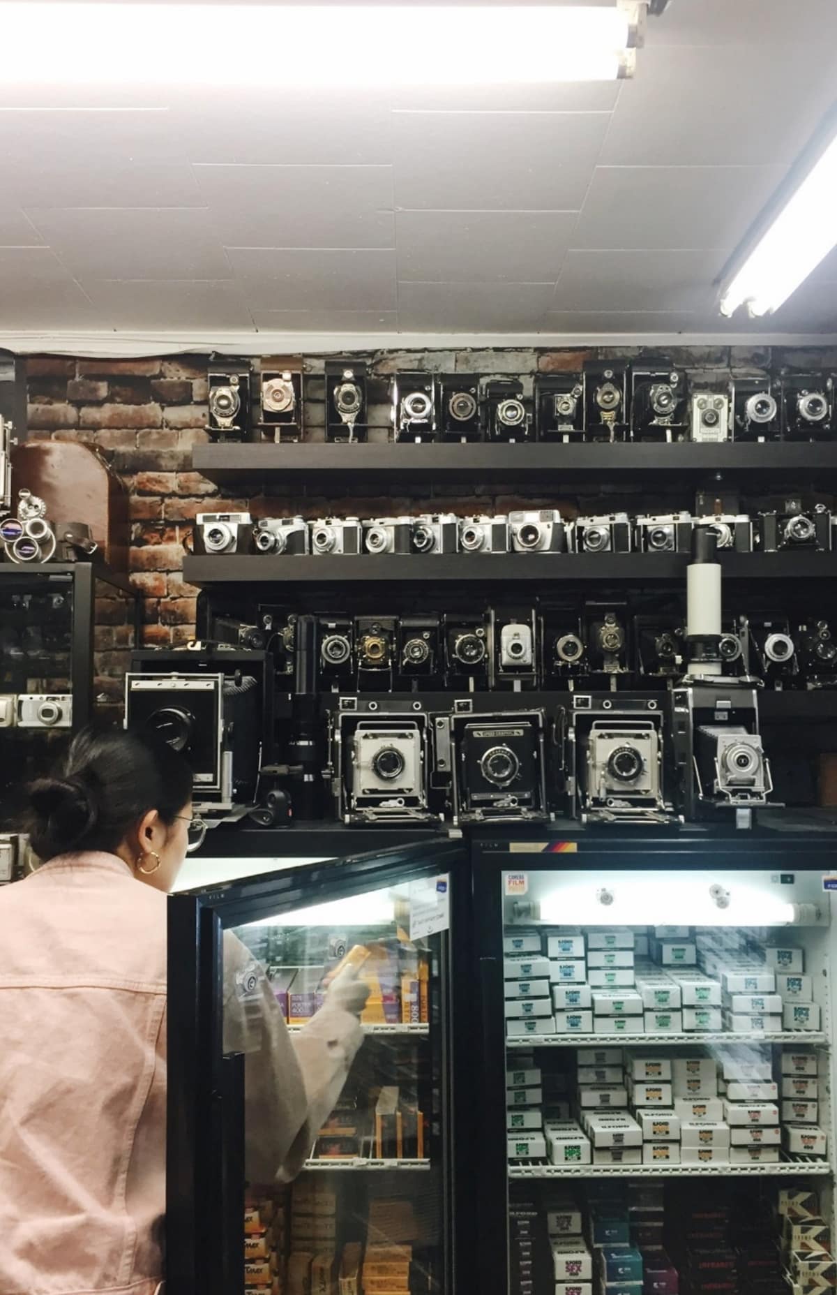 image description: a woman is seen from behind, reacing into a glass sales case, surrounded by vintage cameras.
