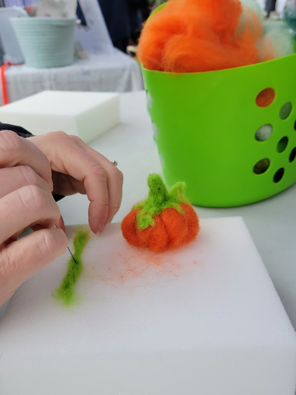 Image description: Two white hands working on needle felting. A needle-felted pumpkin is to hand.