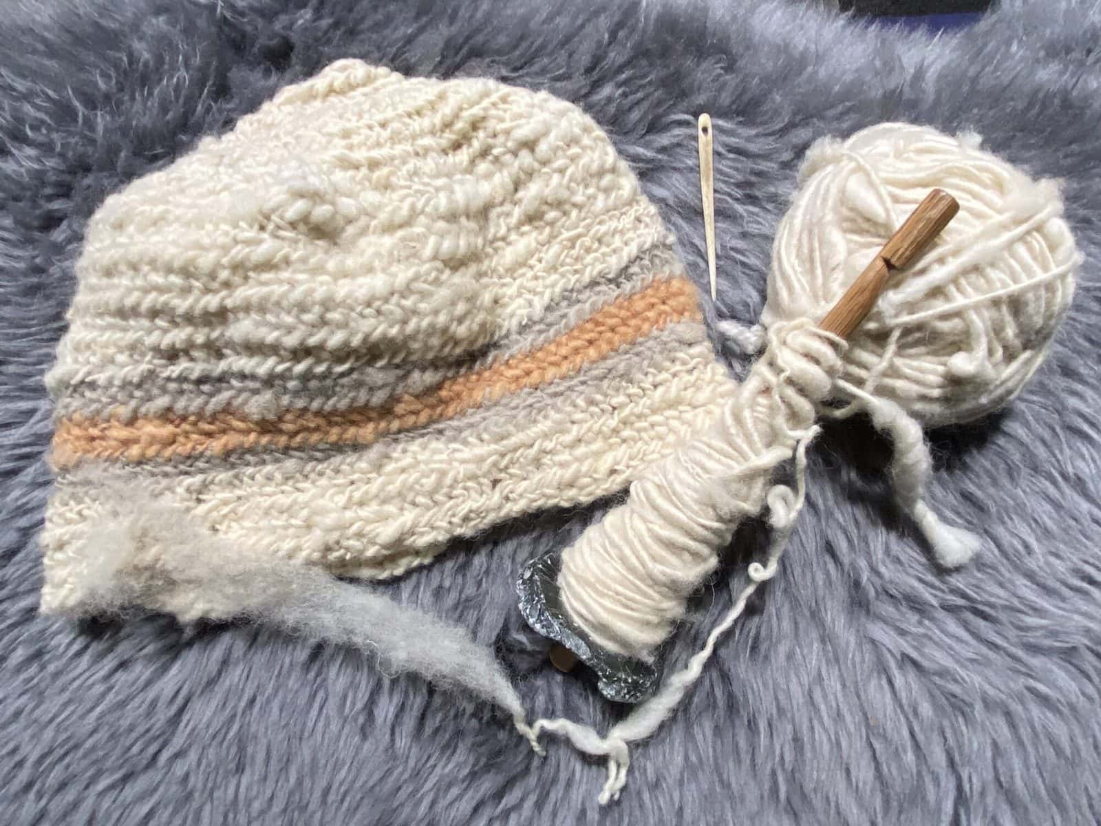 image description: a partially completed hat, beside a ball of handspun yarn and a drop spindle full of wool