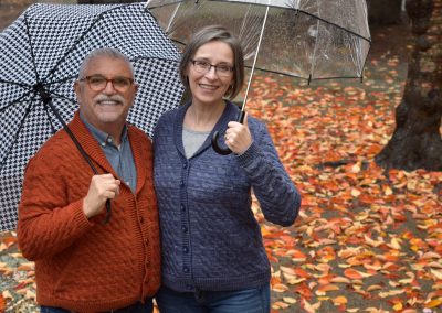 Image description: Man and woman hold umbrellas, with fall leaves in the background.