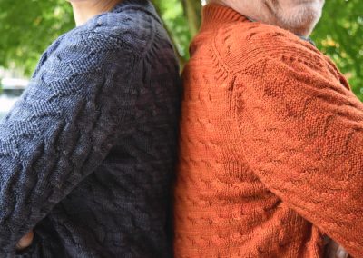 Image description: Person in blue sweater and person in orange sweater standing back to back, seen from the side with shoulders and sleeves visible.