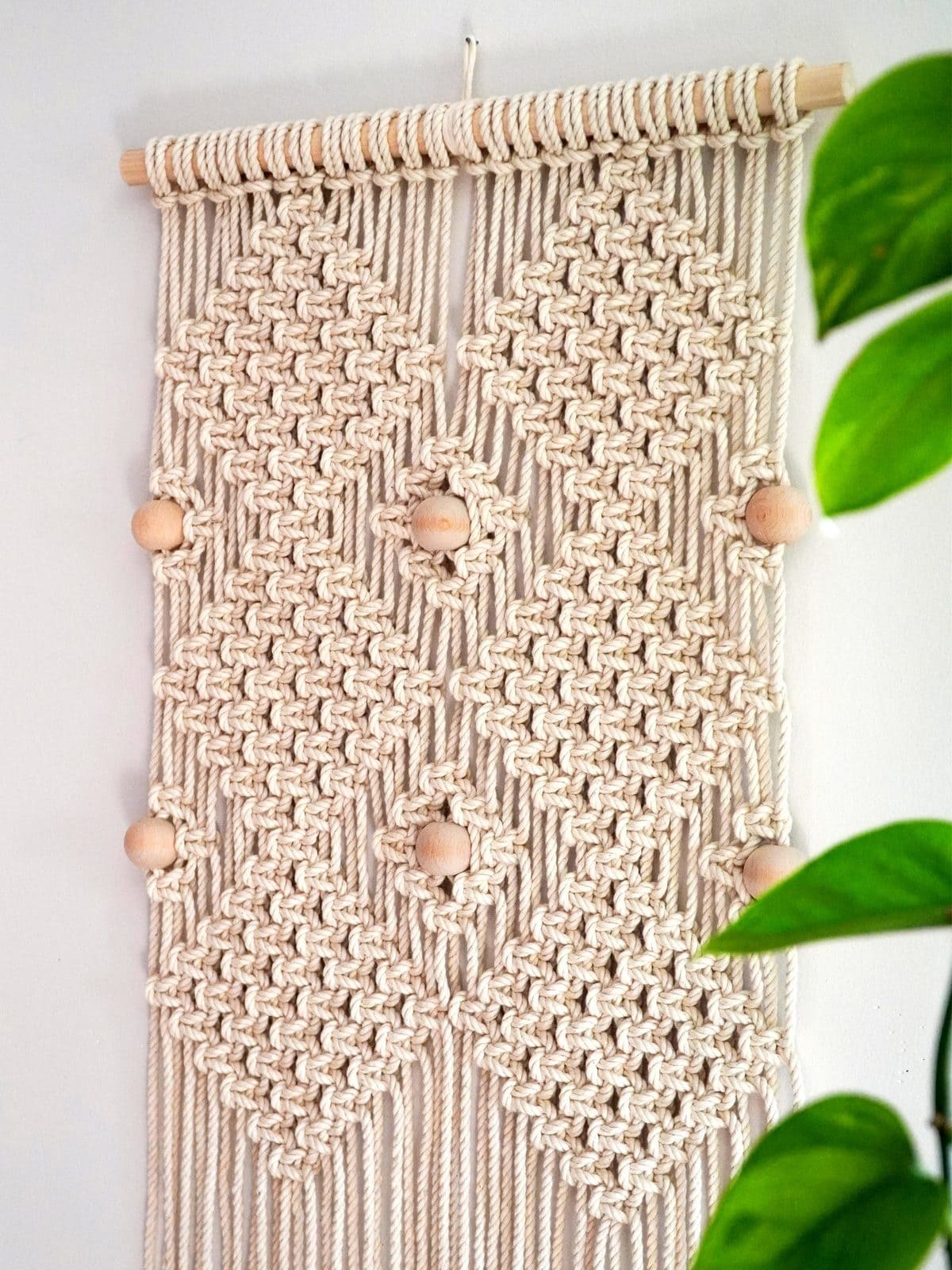 image description: a macrame wallhanging, light coloured rope with wooden beads