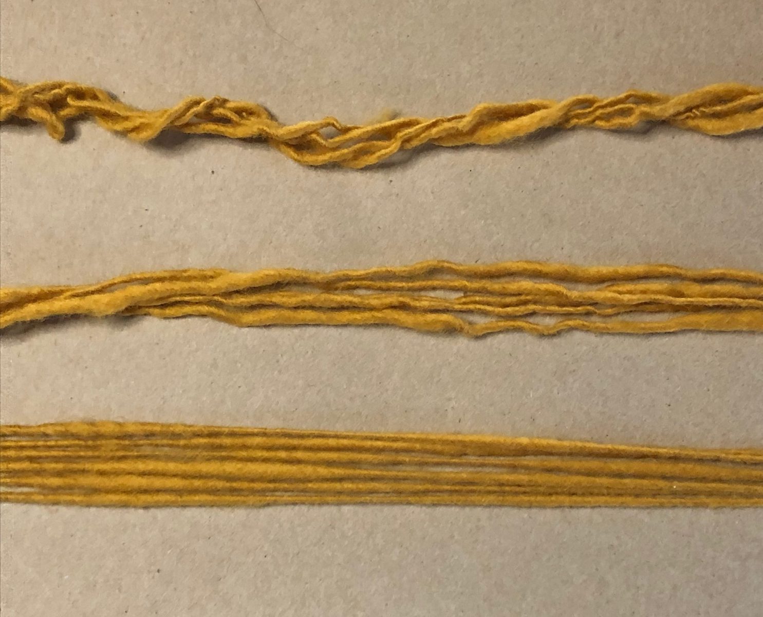 image description: close up of three different groups of yarn strands; the upper ones are very kinky and coiled; the middle ones less so; the bottom ones are very smooth