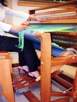 image description: a shot of a woman sitting at a large weaving loom; she is weaving stiletto heeled shoes