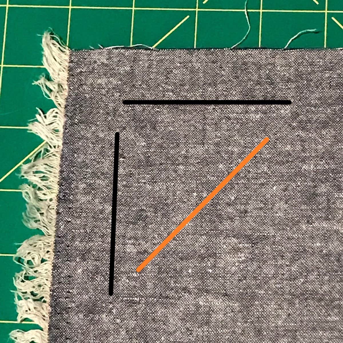 image description: a small piece of fabric, with raw edges visible; an orange line is draw on top, at a 45 degres angle to the edges; two black lines follow the lines of the edge, they are perpendicular to each other