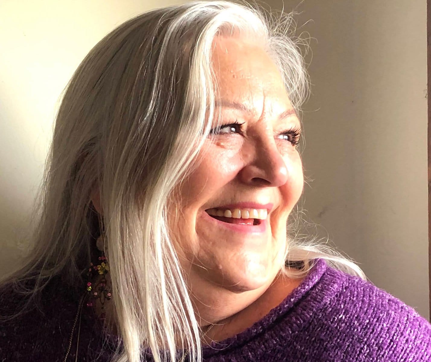 image description: a three-quarters portrait of white woman with long grey hair; she is smiling